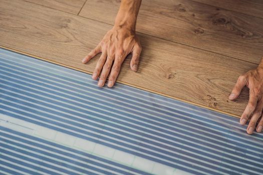 Man installing new wooden laminate flooring on a warm film floor. Infrared floor heating system under laminate floor.