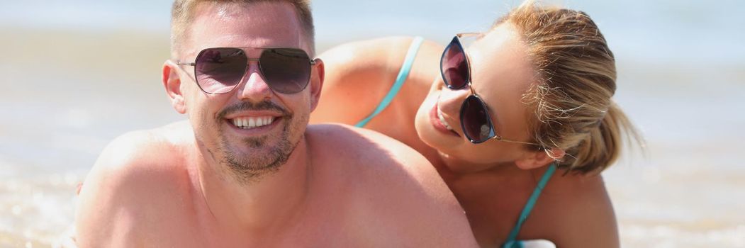 Young happy man and woman in sunglasses lying on seashore. Honeymoon concept