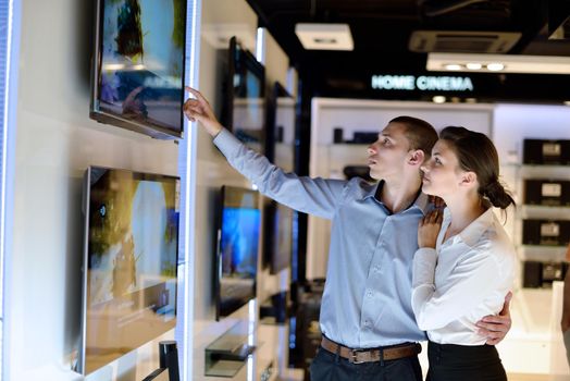 Young couple in consumer electronics store looking at latest laptop, television and photo camera to buy