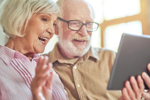 Close up of happy senior husband and wife using digital tablet and chatting during video call at home. Lifestyle concept