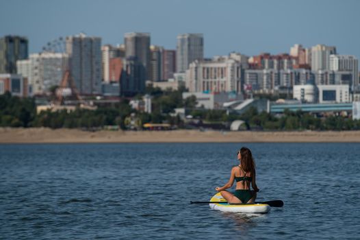 Caucasian woman is riding a SUP board on the river in the city. Summer sport