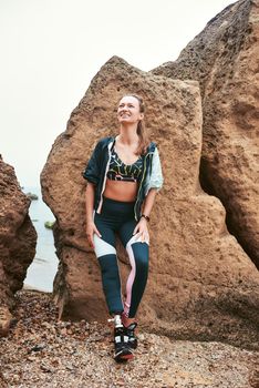 Simply happy. Positive and motivated disabled woman in sports clothing with prosthetic leg leaning against a stone on the beach . Disabled Sportsman. Healthy lifestyle. Happiness concept