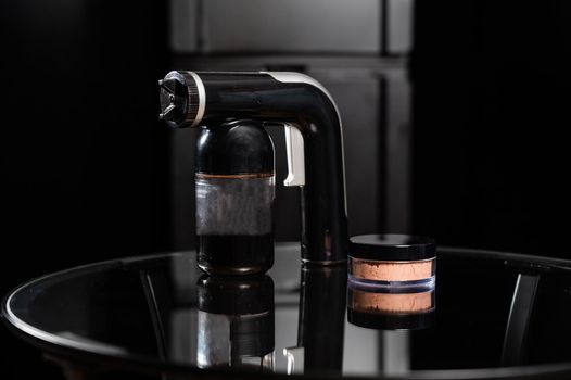 A close-up of the instant tanning equipment. Gun spraying paint for leather and matting body powder on a black background.