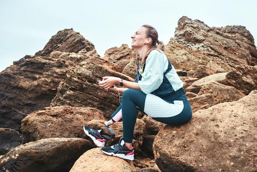 Simply happy. Smiling disabled women in sport wear with leg prosthesis sitting on the boulders, listening music and laughing. Digital concept. Happiness. Disabled Sportsman. Healthy lifestyle.