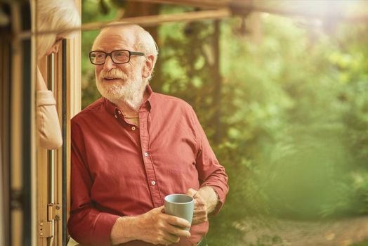 Waist up of smiling gray-haired man talking with his wife near the entrance to their camper van while holding coffee. Travel concept. Copy space