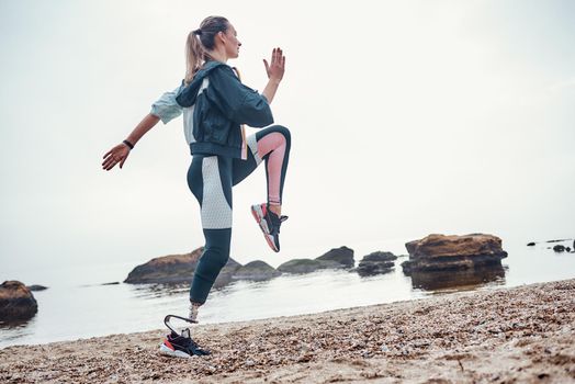 Exercising every morning. Side view of young sporty disabled woman with prosthetic leg is doing sport exercises on the beach. Motivation. Sport concept. Disabled Sportsman