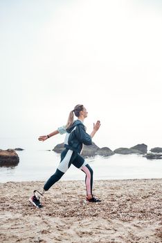 Beach workout. Vertical photo of strong sporty disabled woman with prosthetic leg is running on the beach and doing morning workout. Motivation. Sport concept. Disabled Sportsman