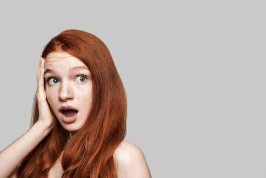 Really Studio shot of cute redhead surprised girl making shocked face while standing against grey background. Human emotions