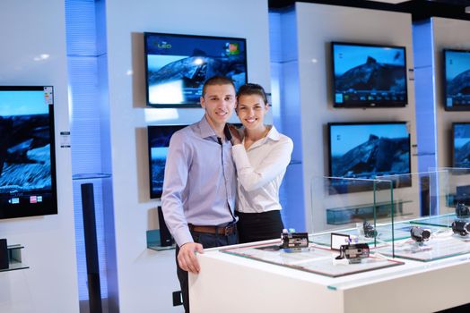 Young couple in consumer electronics store looking at latest laptop, television and photo camera to buy