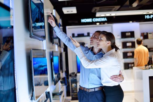 Young couple in consumer electronics store looking at latest laptop, television and photo camera to buy