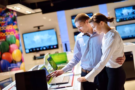 Young couple in consumer electronics store looking at latest laptop, television and photo camera to buy
