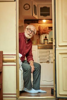 Bearded old man in glasses sitting inside his camper van and looking outdoors while resting. Lifestyle and travel concept
