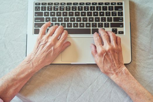 Top view of wrinkled female hands typing on laptop. Domestic lifestyle concept