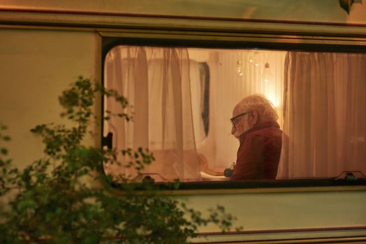 Serious elderly man with glasses holding a map and looking for a new route in the evening in his motorhome. Travel concept