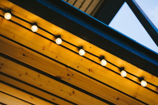 Retro light bulbs on the wooden roof of the coffee shop. Beautiful and eye-catching street decoration of the restaurant. Garland on the wooden ceiling of the terrace.