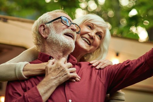 Smiling senior man and woman making selfie and hugging while standing near their motorhome. Lifestyle concept
