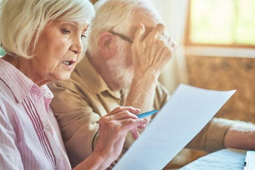 Close up of elderly married couple sitting at table at their house while managing their budget. Family and household concept