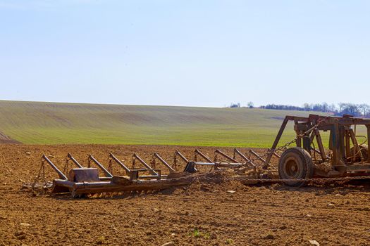 A farmer plows the soil in the field with a chisel plow on a tractor. Agricultural tractor with a plow on field.