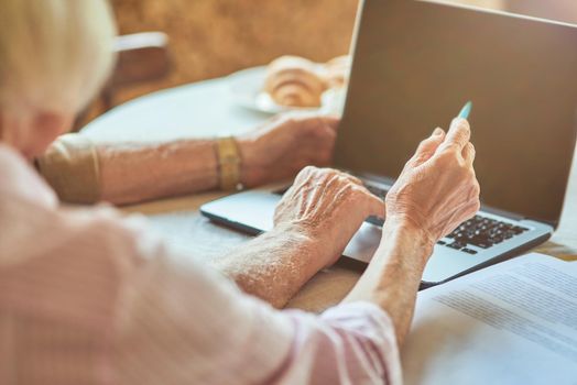 Cropped photo of senior woman holding pen while pointing on laptop screen. Copy space. Family and household concept