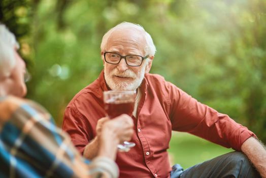 Smiling elderly man holding glass of wine while looking at his wife outdoors. Relationship and family concept