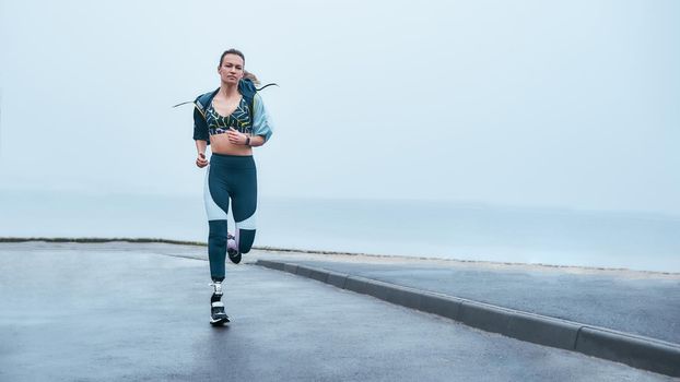 You are stronger than you think. Amazing strong disabled woman in sportswear is running outdoors near the sea. Motivation. Sport concept. Disabled Sportsman