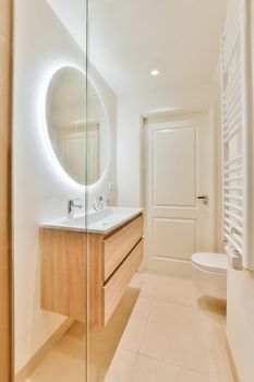 Luxurious bathroom with beige tiled floor and round large mirror with lighting