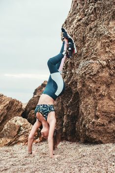 Vertical photo of strong disabled woman working out outdoors and doing handstand exercise on the beach. Sport concept. Disabled Sportsman. Healthy lifestyle