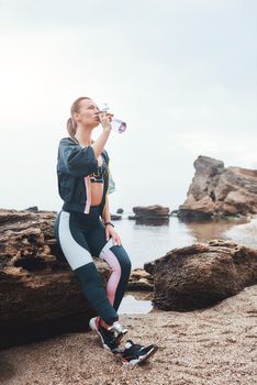 I need some water. Sporty and healthy disabled athlete woman with prosthetic leg drinking water while sitting on the stone at the beach. Disabled Sportsman. Motivation. Sport concept. Taking a break