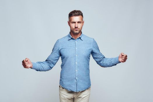 I am strong. Confident and handsome bearded man in casual clothes keeping hands clenched in fists while standing against grey background. Strength and motivation. Studio shot