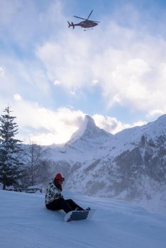 a rescue team with a red helicopter performing the action of rescuing a hurt skier on ski resort