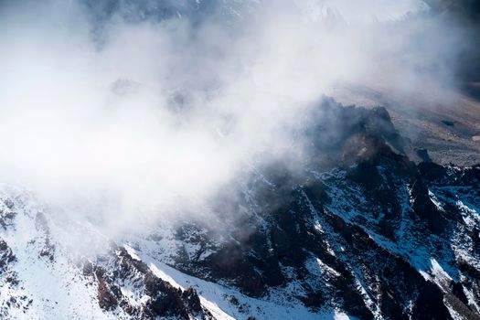 Stunning majestic landscape with snow-capped mountains and glaciers among the clouds on a sunny day.