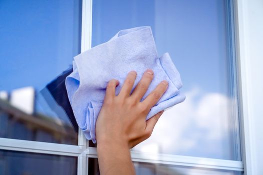 A woman's hand holds a cloth to wipe surfaces and washes the windows of her house to perfect cleanliness and freshness, a creative concept with a close-up of a reflecting sky.