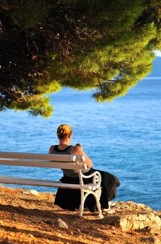 Single woman sitting alone by the beach watching sunset