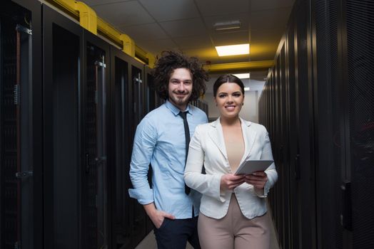 Young IT engineer showing working data center server room to female chief engineer who holding tablet computer