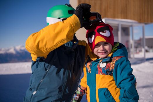 young happy father preparing his little son for the first time on a snowboard during sunny winter day at beautiful  ski resort