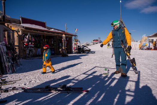 young happy father preparing his little son for the first time on a snowboard during sunny winter day at beautiful  ski resort