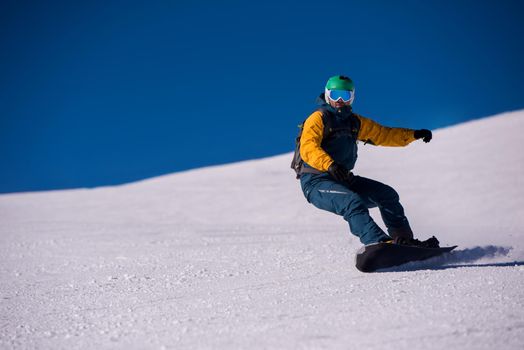 Young freestyle snowboarder running down the slope and ride free style at sunny winter day on Alpine mountains. Winter sport and recreation, leisure outdoor activities.