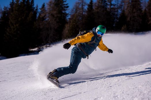 Young freestyle snowboarder running down the slope and ride free style at sunny winter day on Alpine mountains. Winter sport and recreation, leisure outdoor activities.