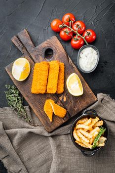 Fried fish finger stick or french fries fish with sauce set, on wooden cutting board, on black background, top view flat lay
