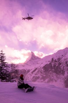 a rescue team with a red helicopter performing the action of rescuing a hurt skier on ski resort