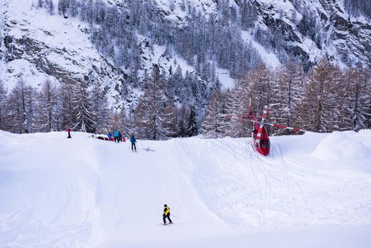 a rescue team with a red helicopter performing the action of rescuing a hurt skier on ski resort