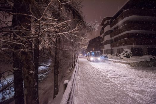 Electric taxi bus on snowy streets in the car-free Alpine mountain village at cold winter night