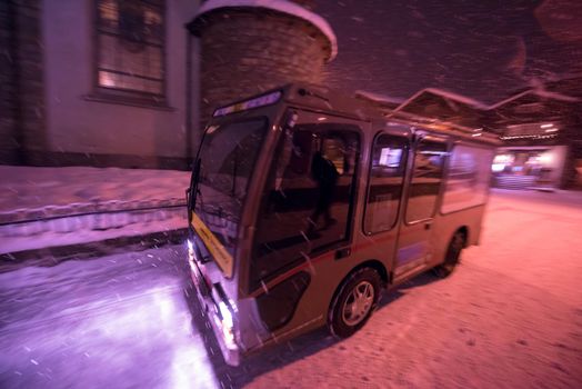 Electric taxi bus on snowy streets in the car-free Alpine mountain village at cold winter night