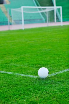 white Soccer ball on grass at goal and stadium in background