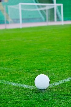 white Soccer ball on grass at goal and stadium in background