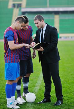 soccer  sport manager in business suit coach and football player on stadium with green grass and white ball