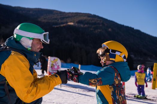 young happy father preparing his little son for the first time on a snowboard during sunny winter day at beautiful  ski resort
