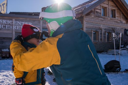 young happy father preparing his little son for the first time on a snowboard during sunny winter day at beautiful  ski resort