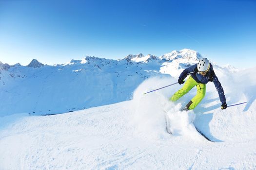 skier skiing downhill on fresh powder snow  with sun and mountains in background