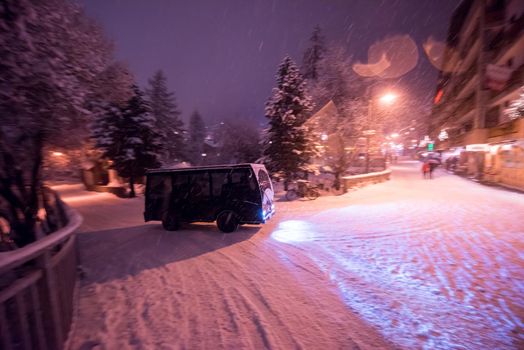 Electric taxi bus on snowy streets in the car-free Alpine mountain village at cold winter night